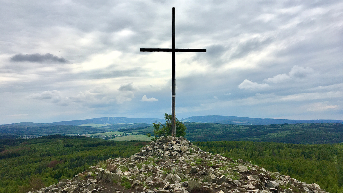 Das Gipfelkreuz auf dem Velký Špičák (Großer Spitzberg). Dahinter rechts der 1.215 Meter hohe Fichtelberg in Deutschland und links der 1.244 Meter hohe Klínovec (Keilberg) in Tschechien. Foto: Chris Bergau